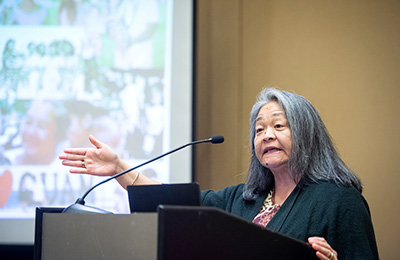 A poster presenter at the AUCD Conference smiles while sitting in front of his poster, talking to another attendee.